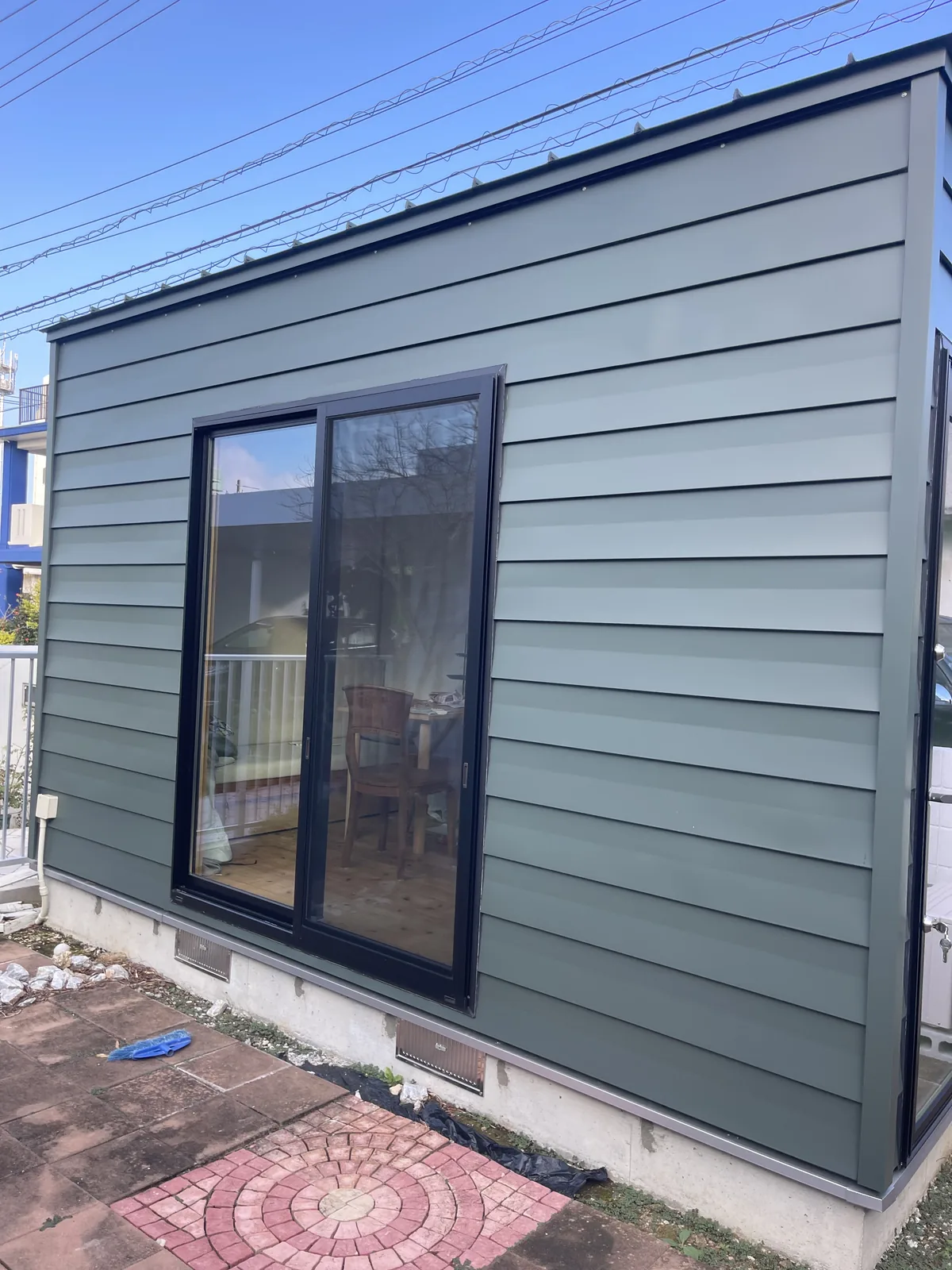 グレーグリーンの外壁に黒い引き違い窓を付けた小屋